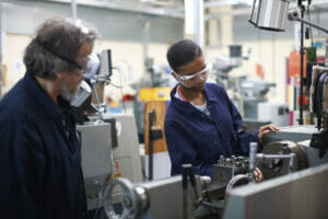 Lecturer teaching student to operate machine in workshop